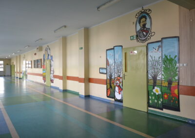 Pusty korytarz szkolny z ilustracjami na ścianach.