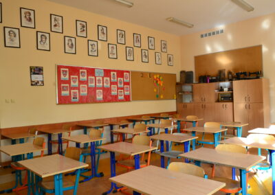 Pusta sala lekcyjna z pojedynczymi ławkami ustawionymi w rzędach.